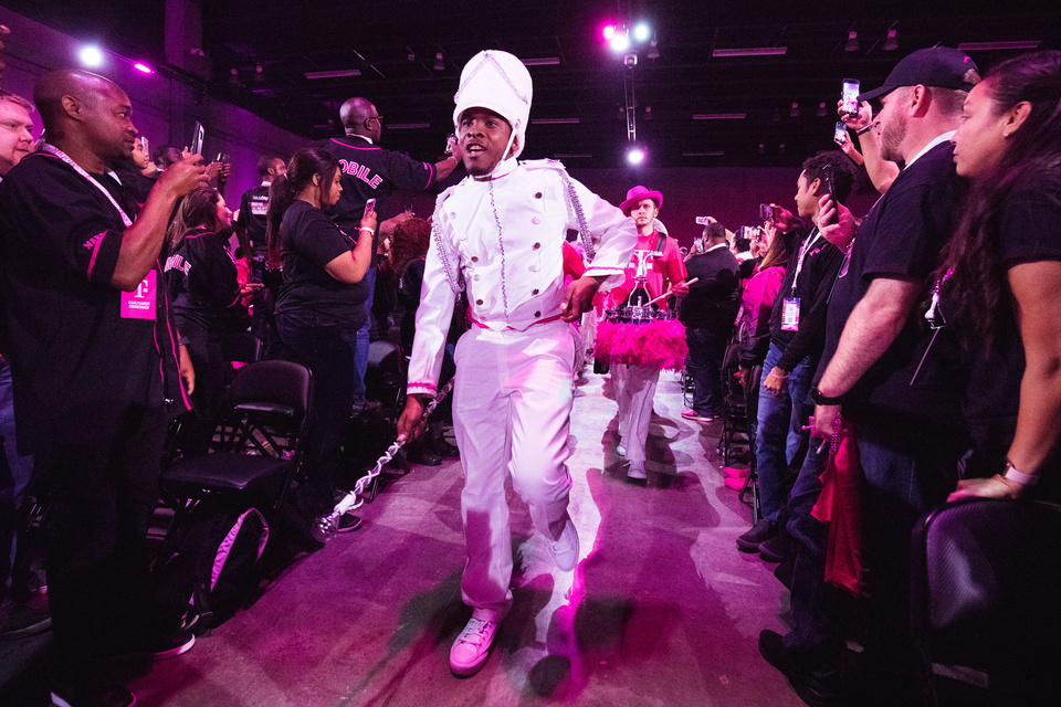 Photo of a marching band performer dressed in white walking down a runway through a crowd.