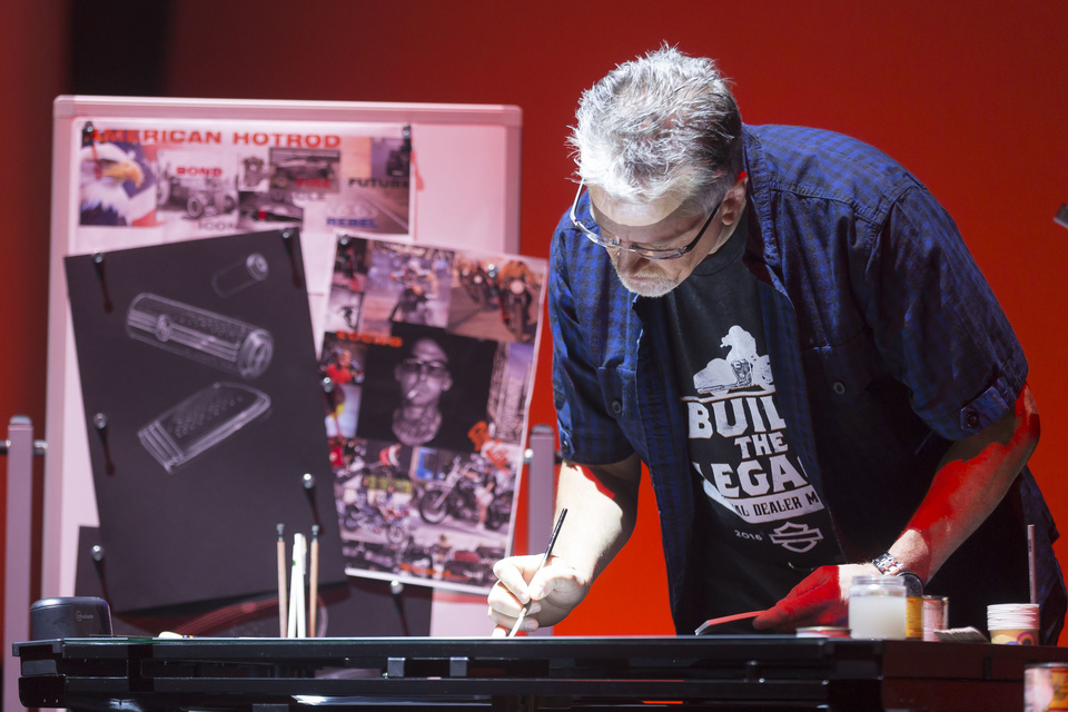 Photo of a person painting on a desk with a Harley Davidson shirt on.