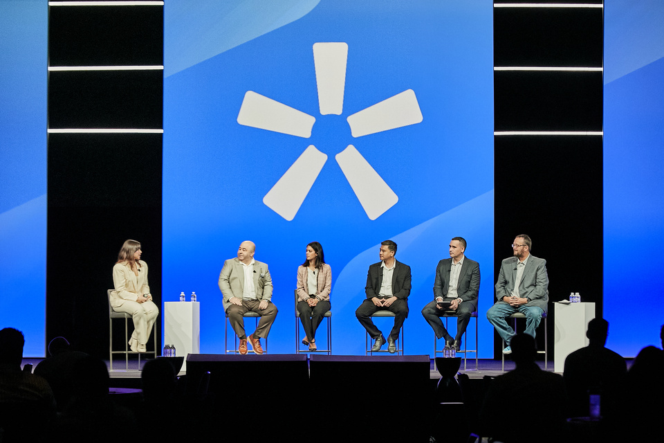 Image of 5 panelists on a stage in front of a blue Orion logo on screen. Panelists are looking towards a moderator 