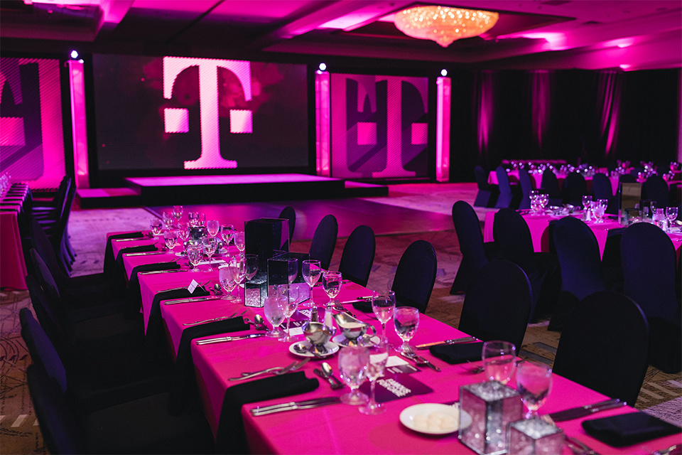 Photo of an empty, magenta themed dining area with a small stage in the background presenting the T-Mobile logo.