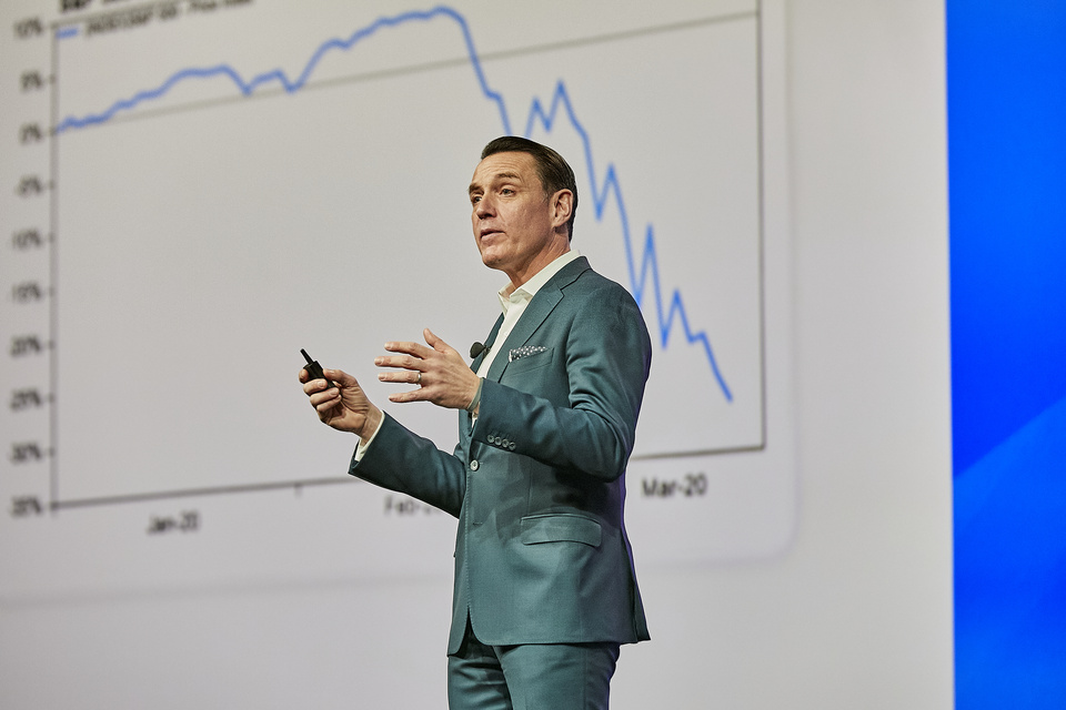 Image of speaker in a suit presenting information in front of a line graph