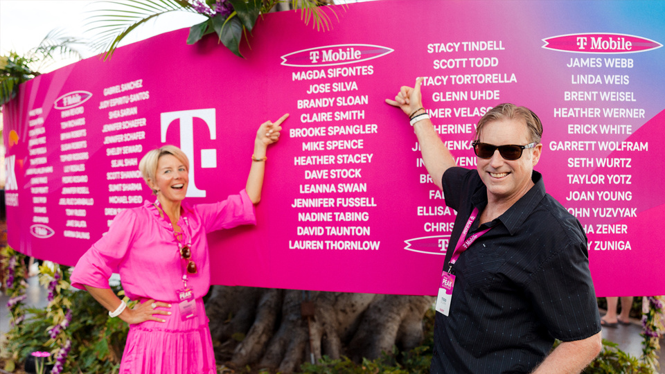 Photo of 2 people pointing at a list of names on a magenta T-Mobile sign