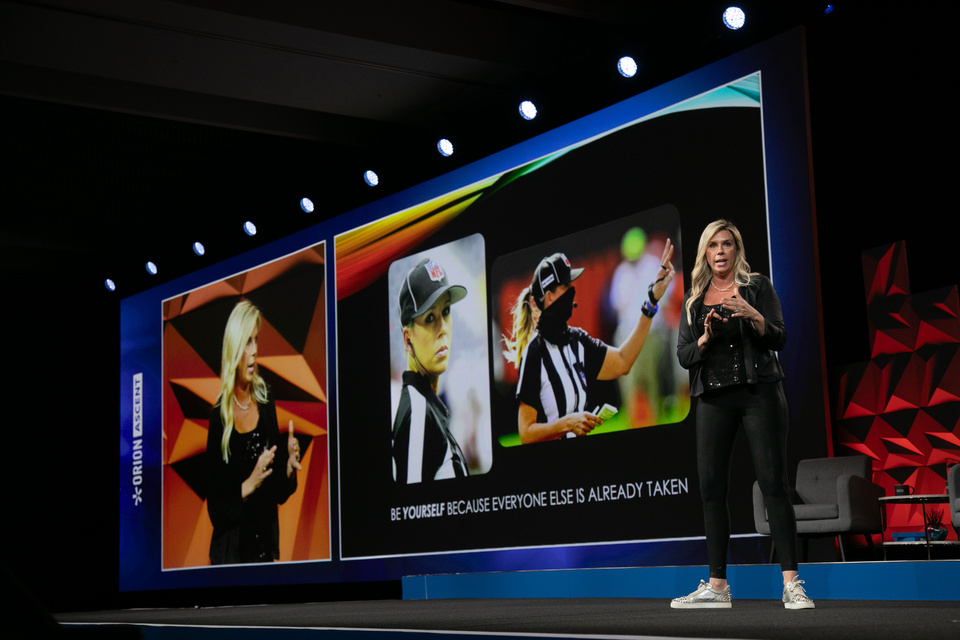 Photo of a female NFL referee presenting information on screen in front of an LED screen