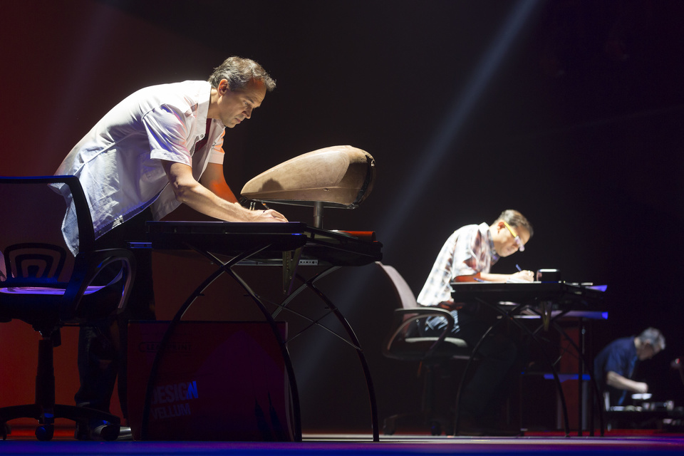 Photo of 3 designers on stage drawing on 3 desks.