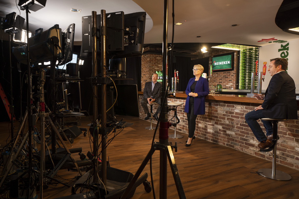 Photo behind the scenes of Lighting equipment setting the scene at a staged bar with Heineken branding and three people.