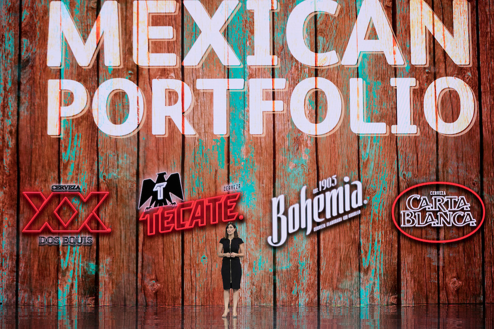 Photo of presenter on stage in a theater in front of an LED screen showing XX logo, Tecate logo, Bohemia logo, and carta blanca logo with the on screen text "Mexican Portfolio."