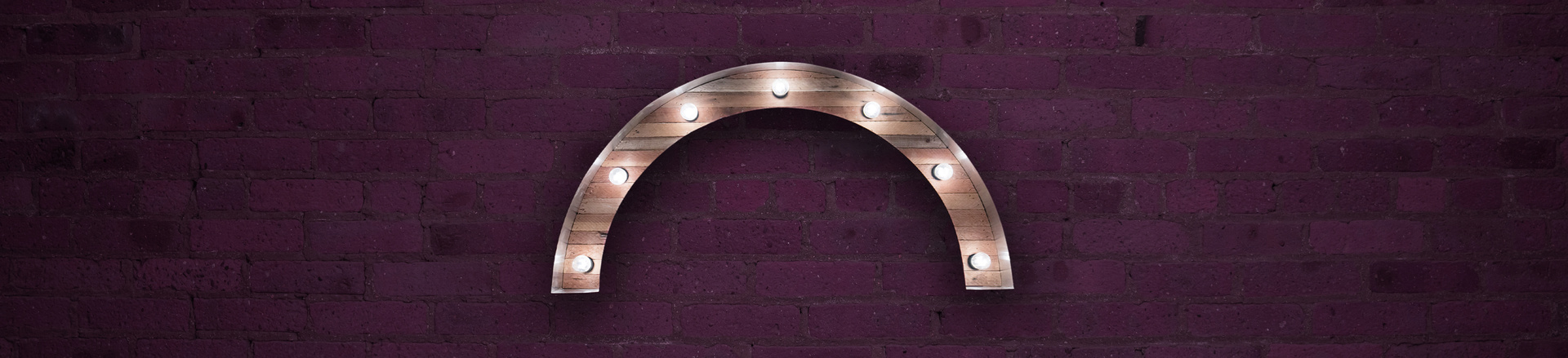 Marquee-style arch Proscenium logo on a plum-colored brick wall background.
