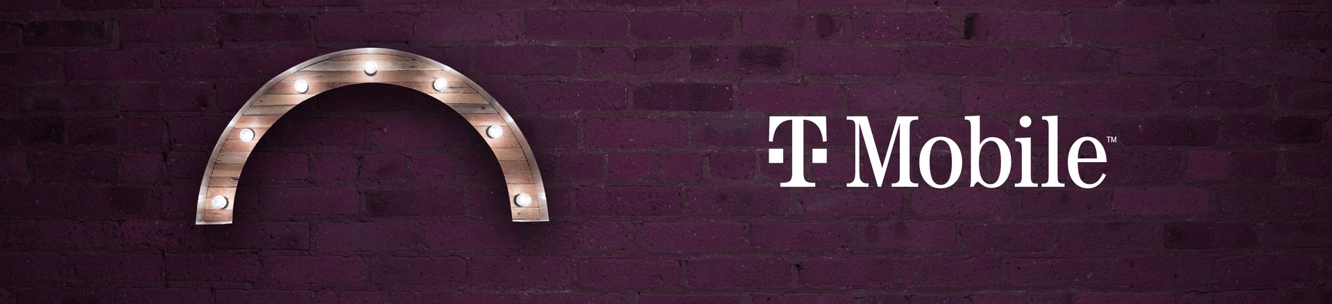 Marquee-style arch Proscenium logo and T-Mobile logo on a plum-colored brick wall background.
