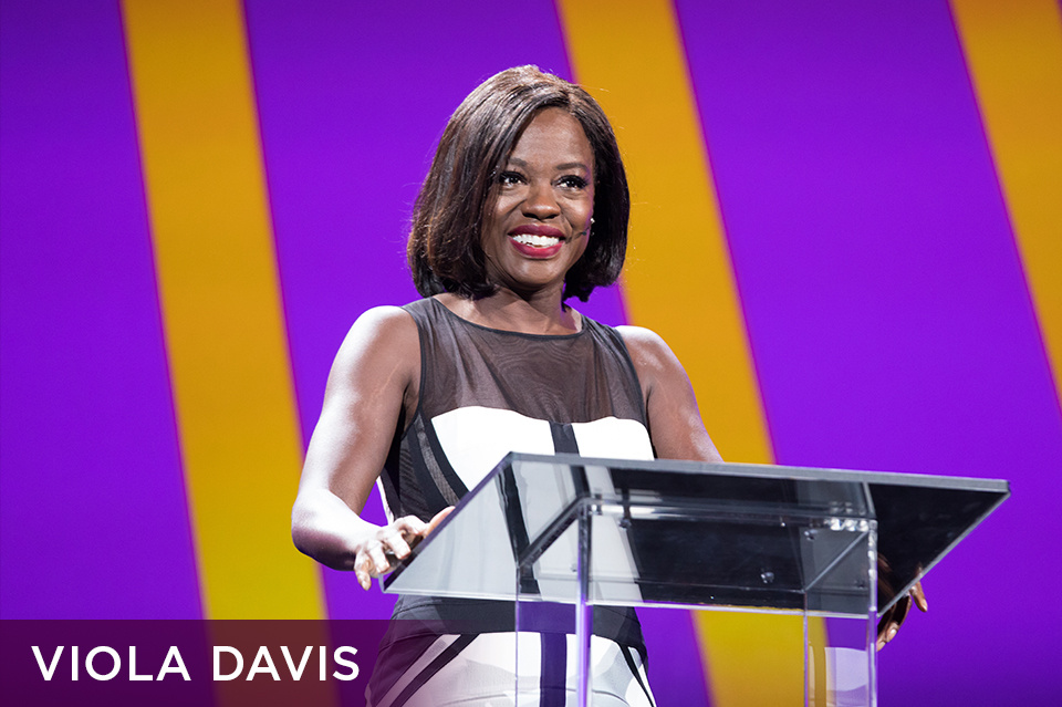 Photo of Viola Davis standing at a clear lectern on stage and smiling. Bottom left plum footer reads "Viola Davis" 