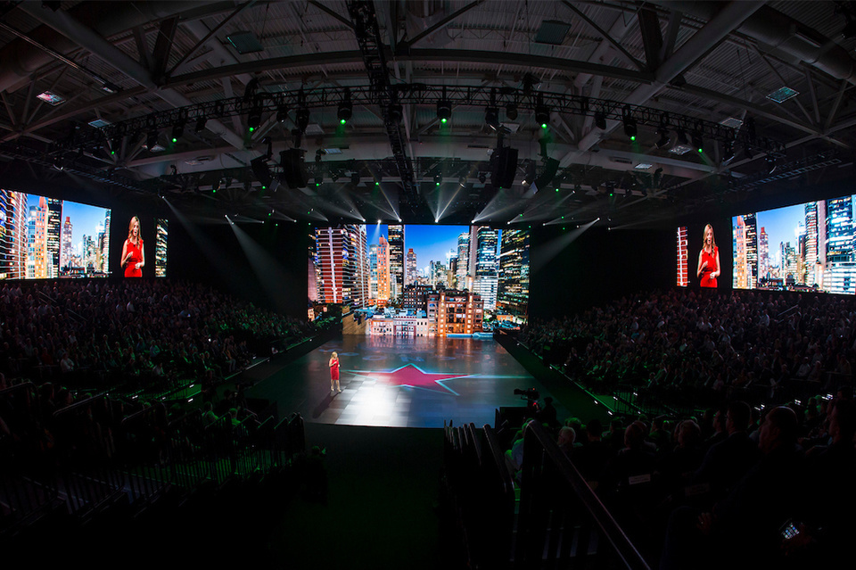 Wide photo of woman standing in front of cityscape background on Heineken logo and speaking to an audience 