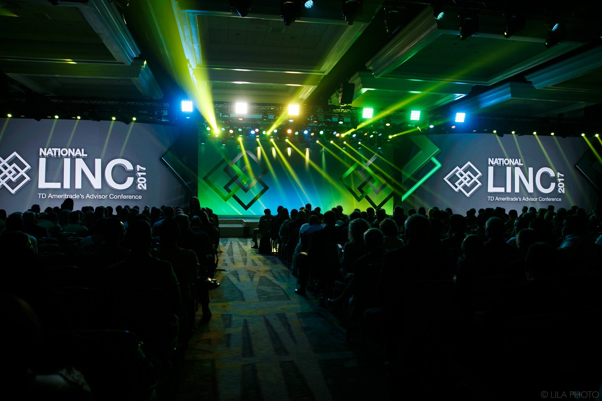 Photo of an empty stage with 2 screens showing National LINC 2017: TD Ameritrade Institutional branding and green lighting