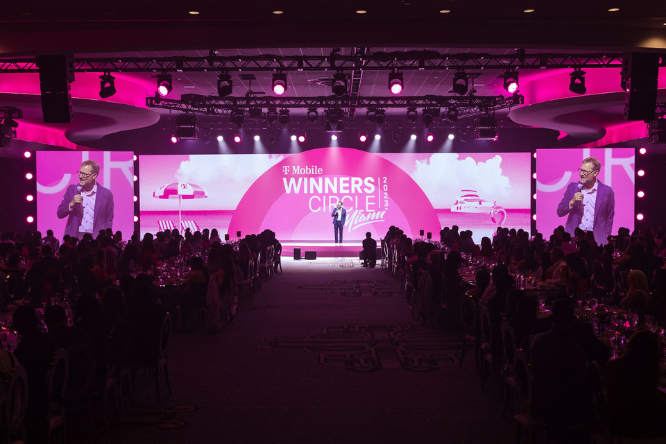 Photo of Mike Sievert Center Stage speaking to an audience in front of a magenta LED screen that reads "T-Mobile Winners Circle 2023 Miami