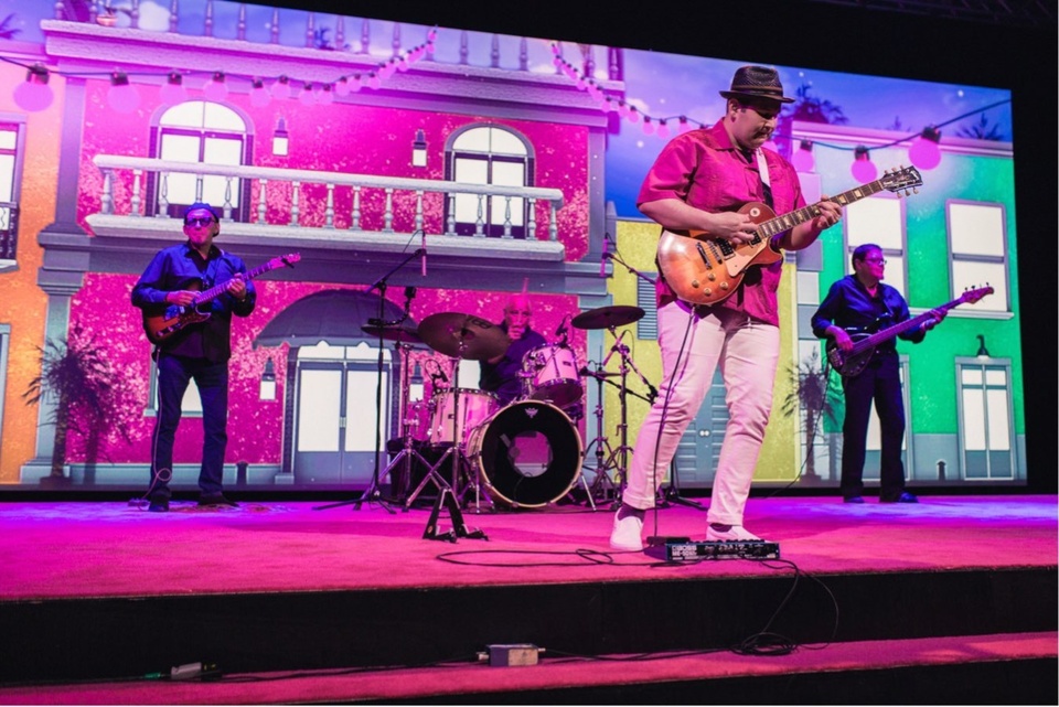 Photo of a rock band performing on a magenta stage.
