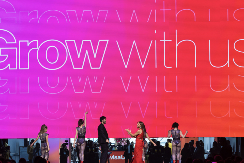 Photo of 5 performers on stage as an LED screen pulls up with the text "Grow with us" on the screen