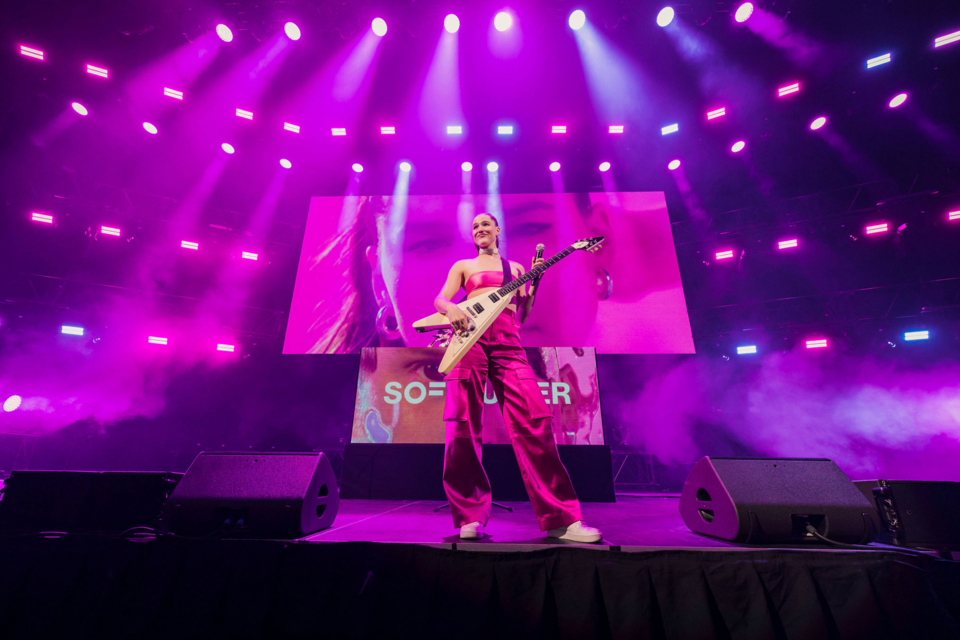 Image of musician Sofie Tukker on stage on a magenta background holding a guitar