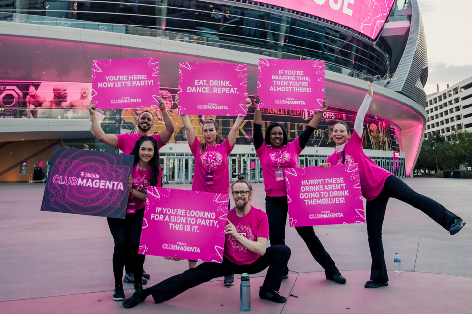 Photo of 6 Employees holding T-Mobile Club Magenta Signs Outside of an Arena