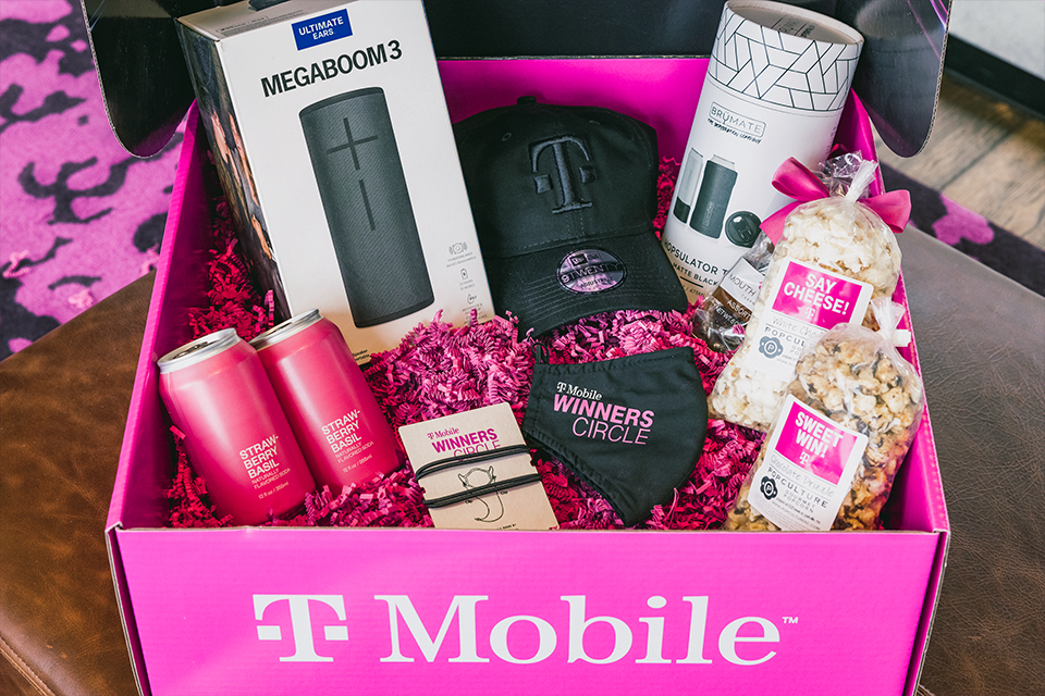 Photo of branded T-Mobile gift box with T-Mobile swag and Megaboom speaker, popcorn, and beverages inside